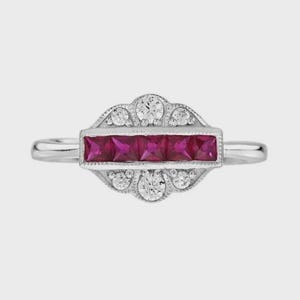 May include: A silver-toned ring featuring a horizontal row of five square-cut vibrant red rubies. The central bar is flanked by a decorative scalloped border containing six small, round, clear white stones arranged in a symmetrical pattern.