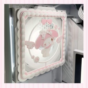 May include: A square computer cooling fan featuring a white scalloped frame with a pink inner border. The centre displays a white and pink character with long ears, a bow, and small wings, surrounded by a circular frame with a bow at the top.