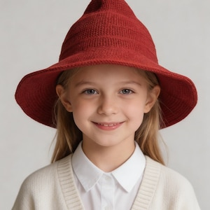 May include: A deep red, pointed, textured knit hat with a wide, slightly downturned brim. The hat features a distinct conical crown shape and a consistent, fine-gauge woven pattern throughout the fabric, providing a structured yet flexible appearance.
