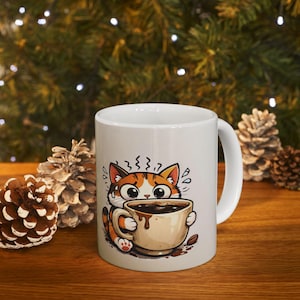 Può includere: Tazza da caffè in ceramica bianca con un gatto dei cartoni animati con pelo arancione e marrone, che tiene in mano una tazza di caffè beige piena di liquido marrone scuro. Il gatto ha grandi occhi e un'espressione preoccupata. La tazza è su una superficie di legno con pigne sullo sfondo.