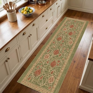 Puede incluir: Una alfombra de pasillo rectangular larga con un fondo verde salvia y un patrón botánico repetitivo de granadas, hojas y pequeñas flores de color marrón rojizo, enmarcada por un borde decorativo con un diseño floral intrincado a juego.