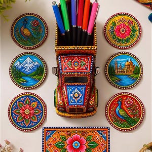 Pu&ograve; includere: Un portapenne in legno dipinto a mano a forma di camion contenente sei penne colorate, circondato da sei sottobicchieri circolari e uno rettangolare. Ogni oggetto presenta motivi vivaci e complessi di fiori, pavoni, montagne e architetture.