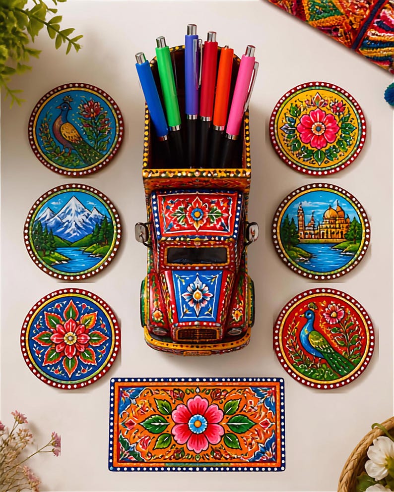Pu&ograve; includere: Un portapenne in legno dipinto a mano a forma di camion contenente sei penne colorate, circondato da sei sottobicchieri circolari e uno rettangolare. Ogni oggetto presenta motivi vivaci e complessi di fiori, pavoni, montagne e architetture.