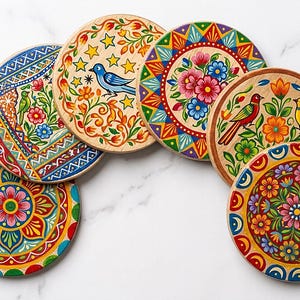 Pu&ograve; includere: Un set di sei sottobicchieri circolari in legno con vivaci disegni dipinti a mano. Ogni sottobicchiere presenta motivi colorati unici, tra cui disegni floreali, uccelli stilizzati, stelle e bordi geometrici nei toni del rosso, blu, giallo e verde.