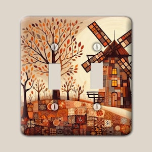 Puede incluir: Una placa rectangular para interruptor doble con una escena impresa de un molino de viento y árboles en colores otoñales. El diseño incluye un suelo estilo patchwork con varios patrones geométricos en tonos naranja, marrón y crema.