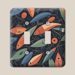 May include: A double light switch wall plate featuring a repeating pattern of stylized fishing lures and hooks in shades of orange, blue, and sage green against a dark charcoal background, secured with four visible silver-toned metal screws.