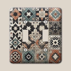 May include: A double light switch wall plate featuring a grid of square tiles with geometric patterns in shades of terracotta, teal, black, and cream. The rectangular plate includes two vertical cutouts for switches and four metal mounting screws.