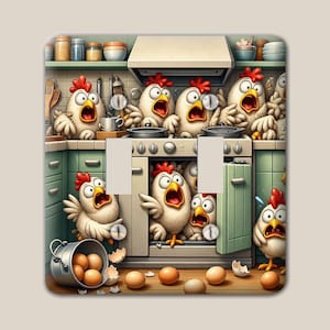 May include: A square light switch cover plate featuring a cartoon illustration of white chickens with red combs in a kitchen. The chickens have wide, surprised eyes and open beaks. There are brown eggs scattered on the floor and in a metal bucket.