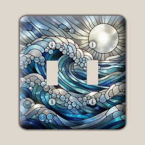 May include: A double light switch cover plate featuring a stained glass style design of a large ocean wave crashing under a bright sun. The artwork uses shades of blue, white, and silver with distinct segmented lines and circular patterns.