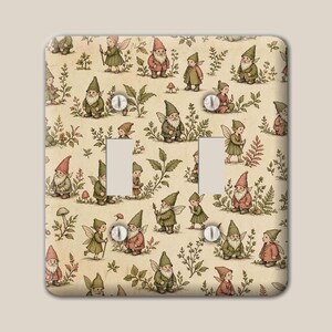 May include: A double light switch cover plate featuring a repeating pattern of gnomes and fairies in muted green, red, and brown tones on a cream background. The rectangular plate includes two vertical rectangular cutouts and four screw holes.