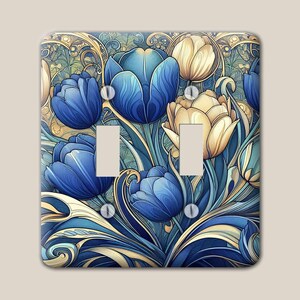 May include: A double light switch cover plate featuring a detailed illustration of blue and cream-coloured tulips with swirling, ornate golden-yellow foliage patterns. The rectangular plate has two vertical rectangular cutouts and four screw holes.