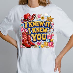 May include: A white t-shirt featuring a colorful graphic print with the text I KNEW IT, I KNEW YOU Y'ALL. The design includes red cowboy boots, a red cowboy hat, a sheriff badge, pink bows, smiley faces, stars, hearts, and alphabet blocks.