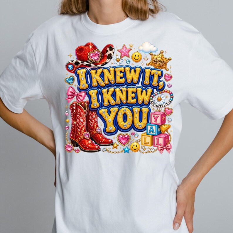 May include: A white t-shirt featuring a colorful graphic print with the text I KNEW IT, I KNEW YOU Y'ALL. The design includes red cowboy boots, a red cowboy hat, a sheriff badge, pink bows, smiley faces, stars, hearts, and alphabet blocks.