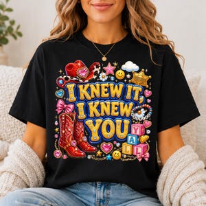 May include: A black t-shirt featuring a colorful graphic print with the text I KNEW IT, I KNEW YOU. The design includes red cowboy boots, a red cowboy hat, a sheriff badge, pink blocks spelling YALL, smiley faces, hearts, and stars.