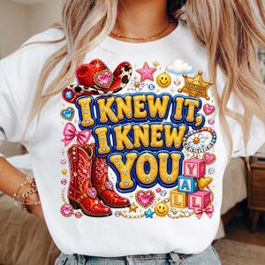 May include: A white sweatshirt featuring a graphic print with the text I KNEW IT, I KNEW YOU. The design includes red cowboy boots, a red cowboy hat, a gold sheriff badge, pink bows, smiley faces, stars, hearts, and colorful alphabet blocks.