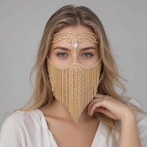 May include: A gold-toned face mask accessory constructed from multiple strands of shimmering rhinestones. The piece features a decorative forehead band with a central teardrop-shaped crystal, connecting to a cascading fringe that covers the nose and mouth.