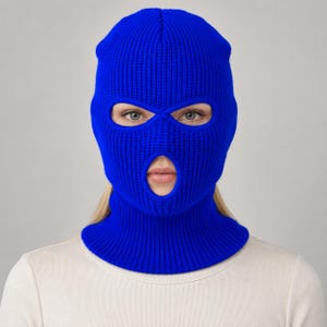 Puede incluir: Un pasamontañas de color azul real brillante hecho de una tela de punto acanalado grueso. La prenda cubre la cabeza y el cuello, presentando dos aberturas para los ojos y una abertura para la boca con un ajuste ceñido y texturizado.