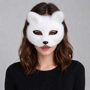 May include: A white faux fur animal mask featuring pointed ears, almond-shaped eye openings, and a small black nose. The mask covers the upper portion of the face, showcasing a soft, textured white material that mimics the appearance of fur.