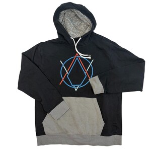 Puede incluir: Una sudadera negra con capucha que presenta un logotipo geométrico en azul y naranja en el pecho. La sudadera incluye un bolsillo canguro gris, puños grises, un dobladillo gris y un cordón blanco. El interior de la capucha tiene un forro gris estampado.