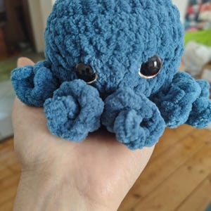 Op de afbeelding: Een handgemaakte blauwe pluche octopus met grote zwarte ogen. De octopus heeft acht gekrulde tentakels en een ronde kop. Het pluche speelgoed is gemaakt van een zacht, getextureerd materiaal en is een schattig, knuffelig speelgoed.