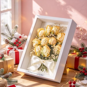 May include: A white shadow box frame containing a bouquet of dried pale yellow roses and baby's breath, tied with a white satin ribbon. The bottom of the frame features the black printed text, Making memories together.