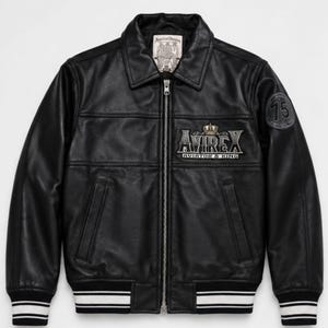 May include: A black leather jacket with a front zipper closure, a collar, and ribbed cuffs featuring white stripes. The chest displays an embroidered patch reading AVIREX AVIATOR & KING with a crown, and a circular patch with the number 75 on the sleeve.