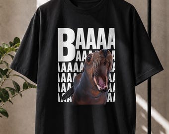 May include: A black short-sleeved t-shirt featuring a graphic print of a sea lion with its mouth wide open. Behind the sea lion, the white text BAAAAA is repeated in a vertical block pattern, filling the background area of the central graphic design.
