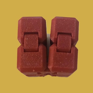 May include: Two connected, red plastic fidget toys. Each piece has a rectangular shape with a hinge in the middle, allowing for movement. The toys are set against a yellow background.