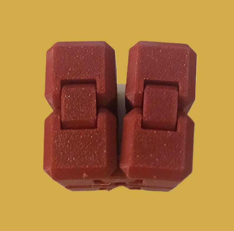 May include: Two connected, red plastic fidget toys. Each piece has a rectangular shape with a hinge in the middle, allowing for movement. The toys are set against a yellow background.