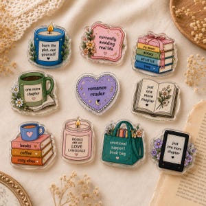 Peut inclure: Un ensemble de neuf broches en acrylique avec des illustrations sur le thème des livres. Les motifs incluent une bougie bleue, un panneau rose, une pile de livres, une tasse verte, un cœur violet, un livre ouvert, une tasse sur des livres, une bougie rose, un sac fourre-tout vert et une liseuse.