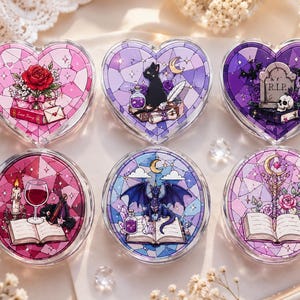 May include: Six compact mirrors featuring stained glass style illustrations. The top row includes a heart-shaped mirror with a rose, a cat with a potion, and a tombstone with the text R.I.P. The bottom row features round mirrors with a wine glass, a dragon, and a staff.
