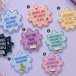 May include: Eight scalloped-edge acrylic coasters featuring book-themed quotes and illustrations. Designs include 'Late Night Readers Book Club', 'Books Are My Happy Place', 'Reading Is My Therapy', 'Books Before People', 'Just One More Chapter', 'Emotionally Attached To Fictional Characters', 'Professional Bookworm', and 'Easily Distracted By Books'.