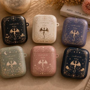 May include: Six rectangular earbud cases in black, cream, purple, sage green, dusty pink, and navy blue. Each case features a gold-toned dragon illustration, celestial motifs, and the printed text "i will not die today" on the front lid.