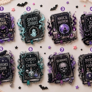 Op de afbeelding: Acht rechthoekige acrylspeldjes met donkere boekomslagen met de titels: Spell Book, Spooky Stories, Magic & Mayhem, Cat Spells, Witches Guide, Curses & Charms, Necromancy en Potions & Poisons. Elk boek is versierd met paarse of blauwe rook.