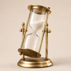 Könnte beinhalten: Eine antike Sanduhr mit Messingrahmen und klaren Glaskolben. Weißer Sand fließt von der oberen in die untere Glaskugel. Die Sanduhr ist geneigt, um ihr Design zu zeigen. Der Sockel und die Oberseite haben dekorative kreisförmige Muster.
