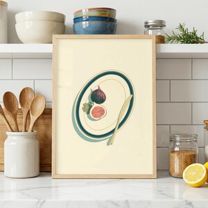 May include: A framed wall art print featuring a light cream background with a centered illustration of a white oval plate with dark teal rims. The plate holds one whole purple fig and one sliced fig, accompanied by a gold-toned butter knife.
