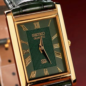 Peut inclure: Une montre-bracelet rectangulaire Seiko Quartz avec un boîtier doré et un cadran vert foncé orné d'un motif ondulé. Le cadran présente des chiffres romains dorés, des aiguilles dorées et un bracelet en cuir vert foncé à motif crocodile.