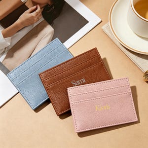May include: Three leather cardholders in pastel colors: light blue, brown, and pink. The brown cardholder has the name "Sami" embossed, and the pink cardholder has the name "Kieris" embossed. Each cardholder has multiple card slots.