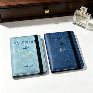 Puede incluir: Dos fundas rectangulares para pasaporte con bandas elásticas. La funda azul claro tiene el texto PASSPORT, un icono de avión, el nombre Miles y travel wallet. La azul oscuro tiene PASSPORT, un icono de avión, June y travel wallet.