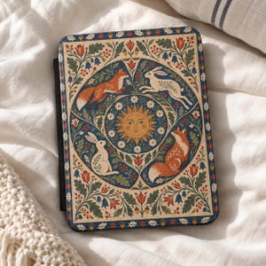 May include: A rectangular e-reader case featuring a central sun illustration surrounded by two foxes and two rabbits. The design includes intricate floral and oak leaf patterns in shades of orange, white, blue, and green on a cream background.