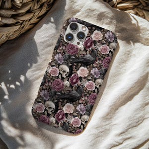 May include: A rectangular smartphone case featuring a detailed pattern of dark purple and light pink roses, black ravens, and human skulls. The design covers the entire back of the case, which includes a cutout for a triple-lens camera system.