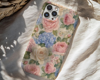 May include: A smartphone case featuring a detailed floral pattern with soft pink roses, cream-colored roses, and clusters of light blue hydrangea blossoms set against a pale background. The case includes a cutout for a triple-lens camera system.