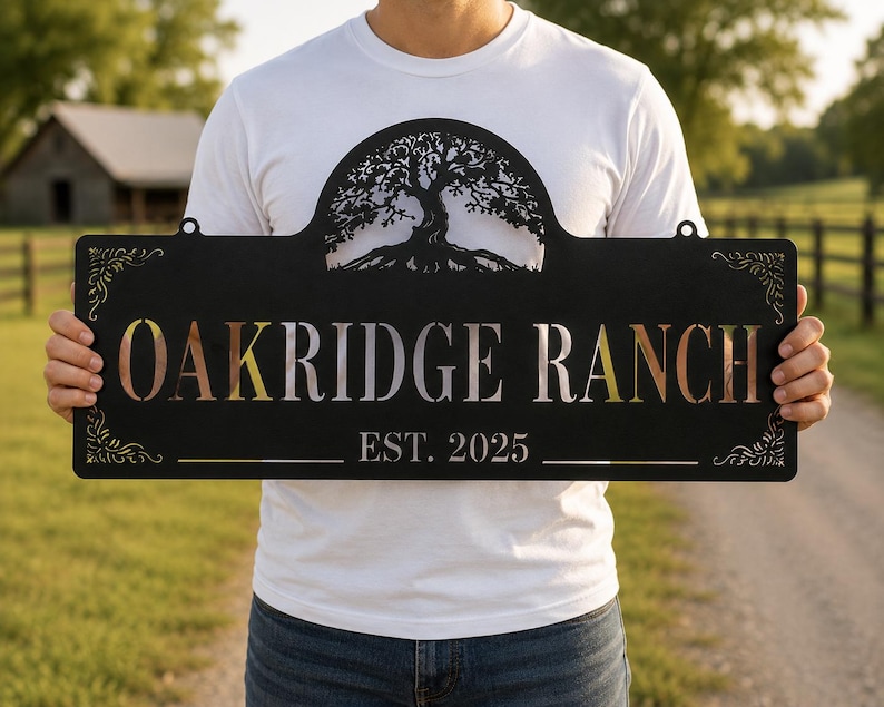 May include: A rectangular black metal sign featuring a laser-cut tree silhouette at the top center. The text OAKRIDGE RANCH is cut out in the center, with EST. 2025 below it. Decorative scrollwork accents the top left and right corners of the sign.