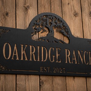 May include: A rectangular black metal sign with an arched top featuring a laser-cut tree silhouette. The sign displays the text OAKRIDGE RANCH and EST. 2025 in a cutout style, revealing a wood-toned background through the lettering and tree.