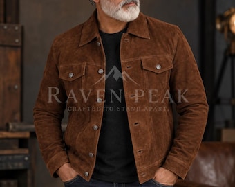 Könnte beinhalten: Eine braune Wildlederjacke mit spitzem Kragen, langen Ärmeln und einer durchgehenden Knopfleiste sowie zwei Brusttaschen. Der Text RAVEN PEAK CRAFTED TO STAND APART ist mittig über einem dunklen Hemd zu sehen.