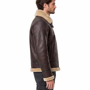 Puede incluir: Una chaqueta de cuero marr&oacute;n oscuro con un cuello grueso de borreguillo beige y ribetes a juego en los pu&ntilde;os y el dobladillo. La chaqueta presenta costuras oscuras visibles a lo largo de las mangas y el torso.