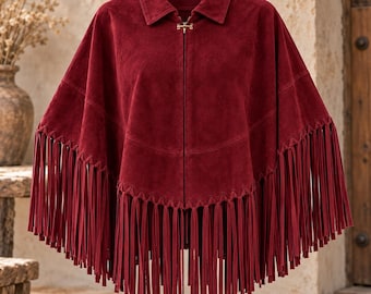 Könnte beinhalten: Ein tiefroter Poncho aus Wildleder mit klassischem Kragen, einem zentralen Reißverschluss mit Metallschließe vorne und langen, dünnen Fransen am Saum. Das Kleidungsstück hat eine strukturierte Schulterpartie und eine weit fallende Silhouette.