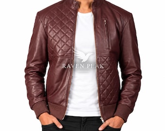 Könnte beinhalten: Eine dunkelburgunderfarbene Lederjacke mit gestepptem Rautenmuster auf der oberen Brust und den unteren Seitenteilen, Stehkragen, vertikaler Reißverschluss-Brusttasche und gerippten Bündchen. Der Text RAVEN PEAK ist in Weiß gedruckt.