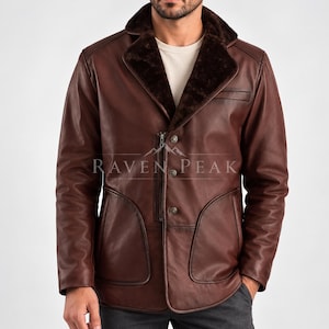Puede incluir: Una chaqueta de cuero marrón con solapa de piel sintética marrón oscuro, un bolsillo vertical con cremallera en el pecho, tres botones frontales y dos bolsillos laterales grandes. El texto RAVEN PEAK está impreso en blanco en la chaqueta.