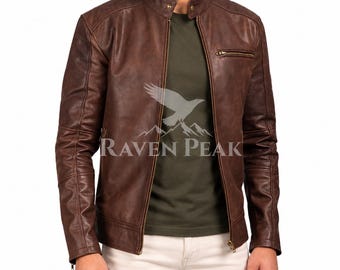 Könnte beinhalten: Eine braune Lederjacke mit Stehkragen, durchgehendem Frontreißverschluss und einer Reißverschlusstasche auf der Brust. Die Jacke hat eine glatte Oberfläche und lange Ärmel. Ein Logo mit Vogelgrafik und dem Text RAVEN PEAK ist sichtbar.